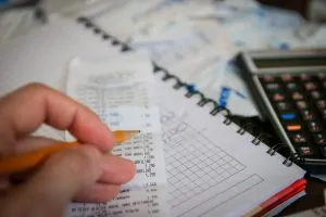 Pessoa anotando a taxação dos produtos importados no caderno
